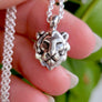 Silver necklace with a lion head pendant held by a hand against a green leafy background