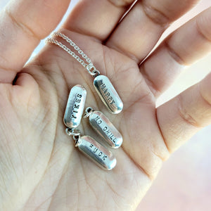 pile of pill necklaces showing yikes, happy, and 'no chill' stamped on the front