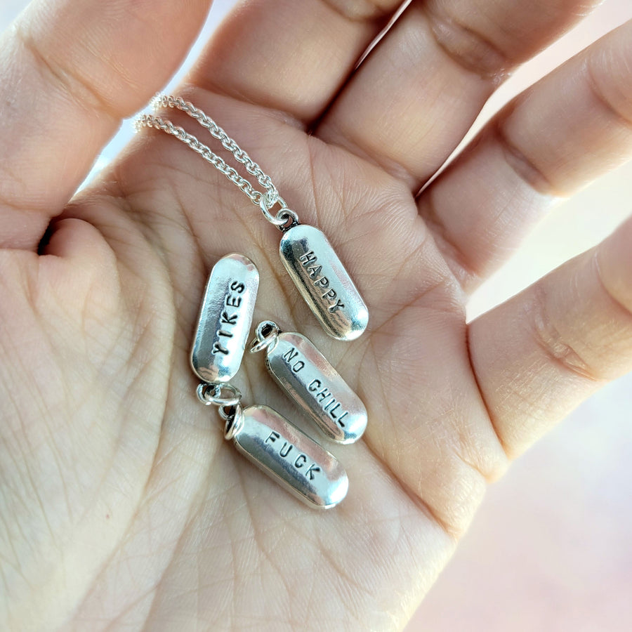 pile of pill necklaces showing yikes, happy, and 'no chill' stamped on the front