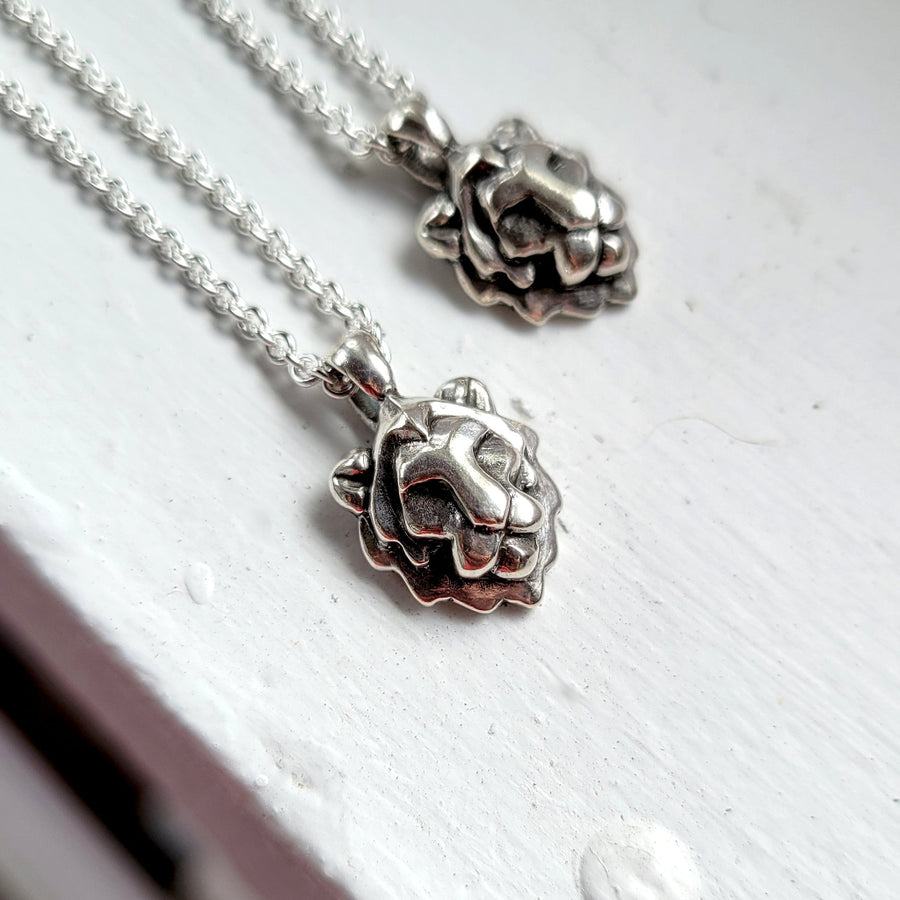 Two silver lion head pendants on silver chains against a white background