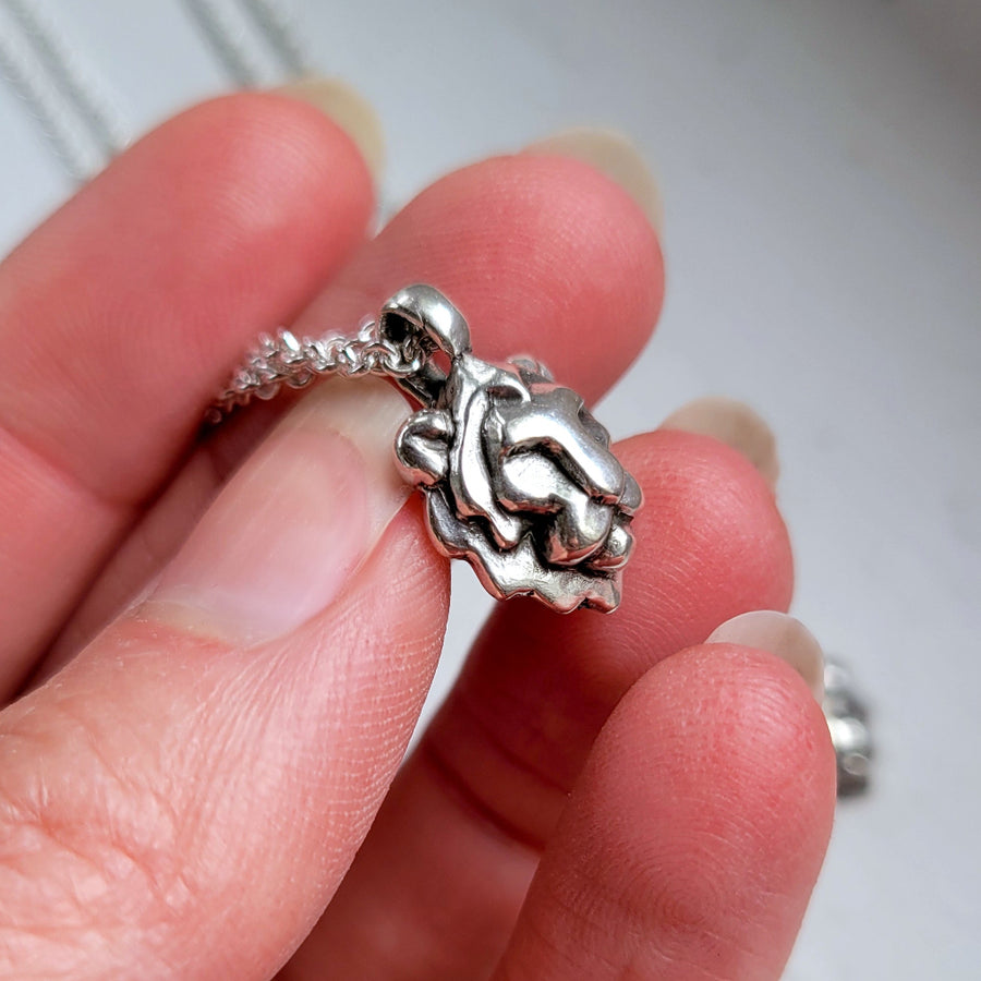 handcrafted Silver lion head pendant held between fingers against a neutral background