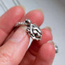 handcrafted Silver lion head pendant held between fingers against a neutral background
